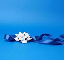 blå silke tunn band vriden och grå skinande rosett på en blå bakgrund foto