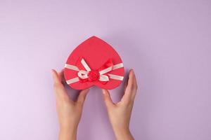 två händer håll en papper stängd röd låda i de form av en hjärta foto