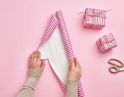två kvinna händer veckla ut en rulla av omslag papper, Nästa till två gåvor, rosa bakgrund foto