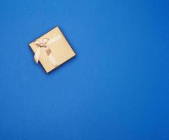 gyllene kartong gåva fyrkant låda bunden med en band på en mörk blå bakgrund, foto