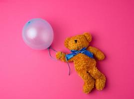 liten brun teddy Björn innehav en blå uppblåst ballong foto