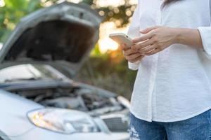 bryta ner, bruten bil, reparera. kvinna användningar mobil telefon kolla upp försäkring premier genom Ansökan på grund av till bil olycka . hitta garage till skaffa sig bil fast under Land Turné, väntar för hjälp, nödsituation. foto