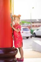 söt liten asiatisk tjej i kinesisk traditionell klänning som ler i templet. Gott kinesiskt nyårskoncept foto