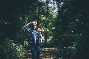 ung kvinna i huvtröja som håller en retro kamera och tar bilder i skogen