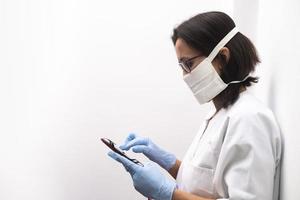 sjuksköterska som bär en mask och blå handskar med hjälp av en tablett på sjukhuset foto
