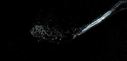 jet av transparent vatten med små droppar och stänk på en svart bakgrund foto