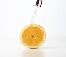 glas pipett med en släppa, Nästa till halv en citron- på en vit bakgrund. frukt syror i kosmetika foto
