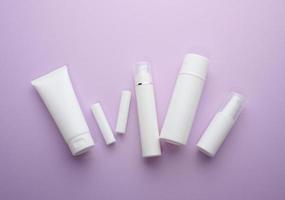 flaska och tömma vit plast rör för kosmetika på en lila bakgrund. förpackning för grädde, gel, serum, reklam och produkt befordran foto