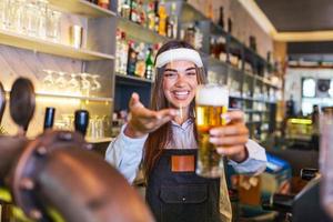 bartender med ansikte skydda covid-19 skydd, tjänande en förslag öl på de bar disken under coronavirus pandemisk, hyllor full av flaskor med alkohol på de bakgrund foto