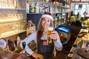 bartender med ansikte sköld, covid-19 skydd, tjänande en förslag öl på de bar disken under coronavirus pandemisk, som visar ok skylt, hyllor full av flaskor med alkohol på de bakgrund foto