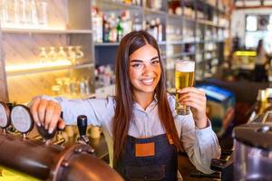 skön leende kvinna bartender tjänande en förslag öl på de bar disken , hyllor full av flaskor med alkohol på de bakgrund foto