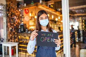 små företag ägare med ansikte mask innehav de tecken för de återöppning av de plats efter de karantän på grund av till covid19. kvinna med skyddande mask innehav tecken vi är öppna, Stöd lokal- företag. foto