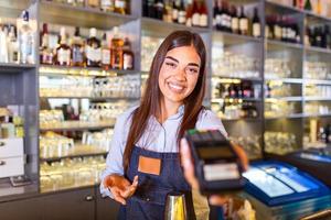 servitris på kontanter disken innehav ett elektronisk kort betalning maskin. stänga upp av ung kvinna innehav trådlös terminal pos på kaffe affär foto