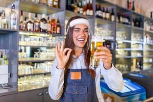 bartender med ansikte sköld, covid-19 skydd, tjänande en förslag öl på de bar disken under coronavirus pandemisk, som visar ok skylt, hyllor full av flaskor med alkohol på de bakgrund foto