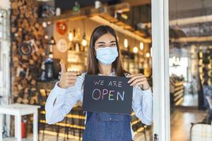 små företag ägare med ansikte mask innehav de tecken för de återöppning av de plats efter de karantän på grund av till covid19. kvinna med skyddande mask innehav tecken vi är öppna, Stöd lokal- företag. foto