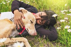 avkopplande kvinna liggande på de gräs kissing henne vinthund hund. foto