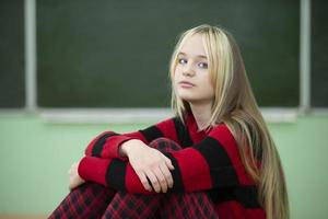 tonåring av senior skola ålder. en Tonårs flicka sitter på de bakgrund av en svarta tavlan och utseende på de kamera. foto