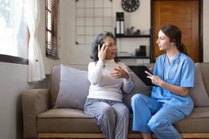 asiatisk sjuksköterska som visar hälsa kolla upp Rapportera till mormor och ger råd. medicinsk assisterad levande besök senior patient på Hem. Hem amning och sjukvård vårdgivare begrepp foto