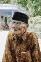 en porträtt av ett gammal asiatisk man bär batik skjorta och glasögon foto