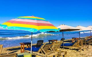 palmer parasoller Sol solstolar strand vågor puerto escondido Mexiko. foto