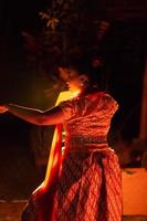 en silhuett kropp av en balinesisk kvinna i en traditionell orange klänning medan dans i främre av de belysning på de mörk natt foto