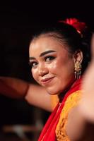 skön ansikte av ett indonesiska kvinna i smink medan dans en traditionell dansa i ett orange kostym under de festival foto