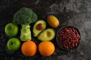 broccoli, äpple, apelsin, kiwi, avokado och bönor på en svart cementgolvbakgrund foto