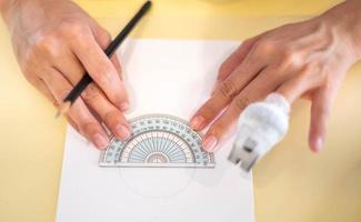 kvinna hand använder sig av en mäta cirkel linjal med en trä penna framställning till dra och skiss på de tömma vit papper. foto