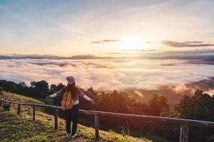 ung kvinna resenärer tittar på soluppgången och havet av dimma på berget på morgonen, resa livsstilskoncept foto