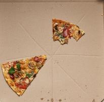 Bitten pizza med rökt korvar, svamp, ost och tomater i en brun kartong låda foto