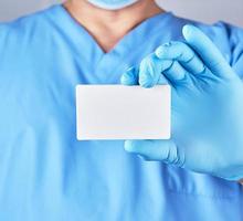 läkare bär blå latex handskar är innehav en tom vit papper företag kort foto