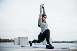 ung sportigt flicka håller på med yoga övningar på kondition matta utomhus nära sjö på dagtid foto