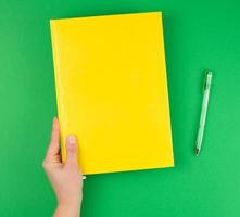 kvinna hand innehav en gul stängd anteckningsbok och penna foto