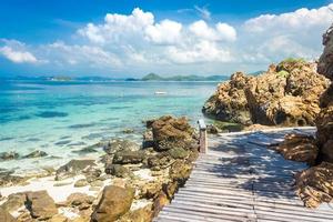 tropisk ö sten- och träbro på stranden med molnig blå himmel foto