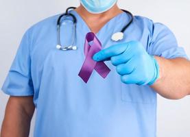 läkare i blå enhetlig och latex handskar innehar en lila band som en symbol av tidigt forskning och sjukdom kontrollera foto