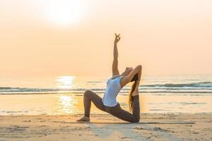 ung asiatisk kvinna håller på med yoga övning på de sand strand i de morgon- på soluppgång. foto