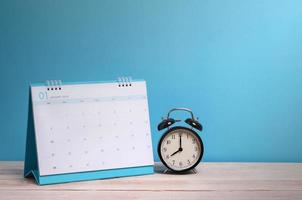 klocka och kalender på skrivbordet med blå bakgrund foto