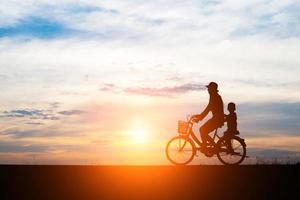 mamma med sitt barn som cyklar vid solnedgången foto