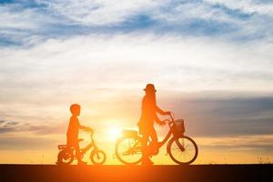 mamma med sitt barn som cyklar vid solnedgången foto