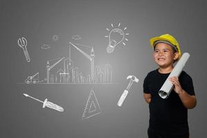 ung pojke som bär en gul ingenjörshatt och husplanidéer på en svart tavla foto