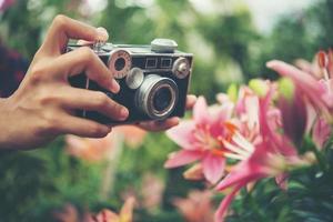 närbild av en kvinnas hand med en vintagekamera som skjuter blommor i en trädgård foto