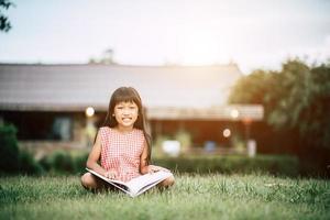 liten flicka som läser en bok i hennes husträdgård utanför