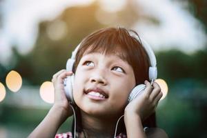 liten flicka som lyssnar på musik i parken med hörlurar foto