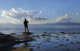 spektakulär landskap på de kust av enoshima, Japan, med en ensam fiskare stående på de kant till de vatten foto