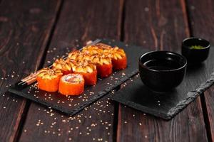 kalifornien sushi rulla med lax, avokado och tobiko kaviar eras på svart styrelse närbild - japansk mat foto