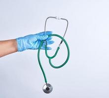 blå steril handskar hand innehav en grön medicinsk stetoskop foto