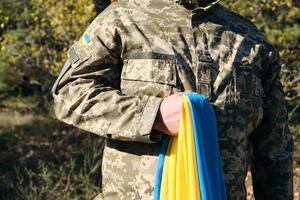 ukrainska soldat innehar i hans hand de gulblå flagga av de stat, han nedtryckt hans hand till hans bröst foto
