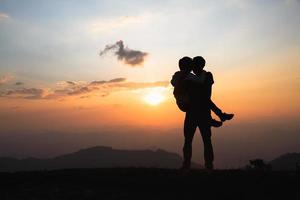 silhuett av en par på de fjäll, en ung romantisk par njut av en skön se av de Sol miljö över de berg, kärlek, hjärtans dag. foto