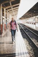 ung hipster man väntar på station plattform med ryggsäck foto