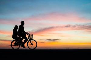 silhuett av ett ungt par på en cykel under solnedgången foto